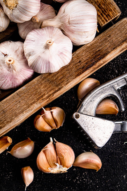 Garlic on a wooden tray with a garlic press. On a black background. High quality photo - Fotografie, Obrázek