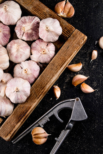 Garlic on a wooden tray with a garlic press. On a black background. High quality photo - Fotoğraf, Görsel