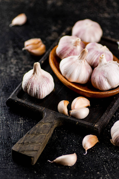 Garlic on a wooden plate on a cutting board. On a black background. High quality photo - Foto, imagen