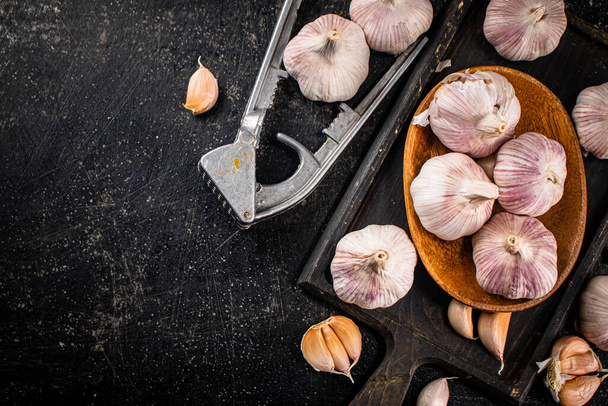Garlic on a wooden plate on a cutting board. On a black background. High quality photo - Zdjęcie, obraz