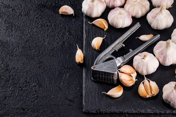 Garlic with a garlic press on a stone board. On a black background. High quality photo - Fotoğraf, Görsel