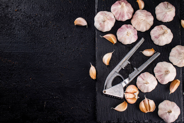 Garlic with a garlic press on a stone board. On a black background. High quality photo - Photo, Image