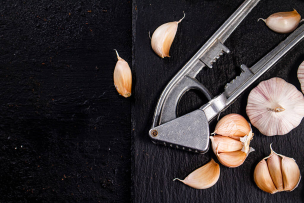 Garlic with a garlic press on a stone board. On a black background. High quality photo - Photo, Image