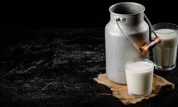 Rustic milk in a can and a glass on the table. On a black background. High quality photo - Фото, зображення