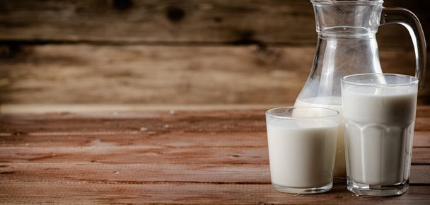 Milk in jugs and glasses. On a wooden background. High quality photo - Foto, Bild