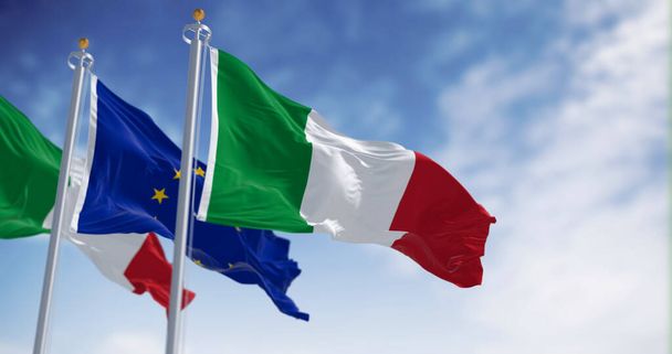 flagi Włoch i Unii Europejskiej powiewające na wietrze w słoneczny dzień. Demokracja i polityka. Państwo członkowskie UE. Ilustracja 3D renderowania. Tkanina trzepocząca - Zdjęcie, obraz