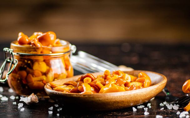 Jar with marinated mushrooms on the table. On a wooden background. High quality photo - Zdjęcie, obraz