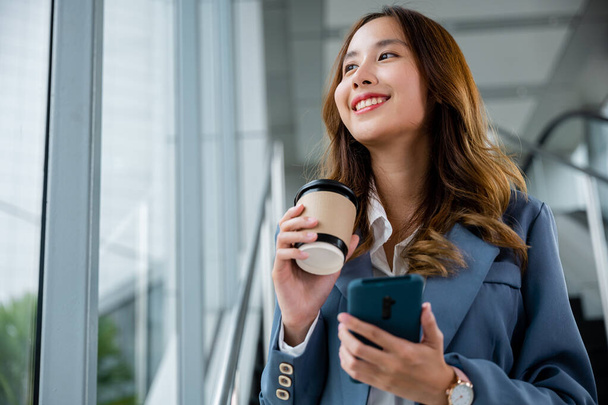Smartwatch y smartphone en la mano, persona femenina mirando el reloj. Moderno fondo de oficina o espacio de trabajo. Ideal para negocios y temas relacionados con la tecnología. - Foto, imagen
