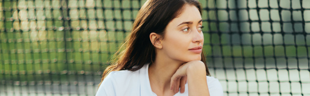kobieta gracz siedzi na korcie tenisowym, zamyślony młoda kobieta z brunetka długie włosy siedzi w białym stroju w pobliżu tenisa netto, niewyraźne tło, Miami, patrząc daleko, baner  - Zdjęcie, obraz
