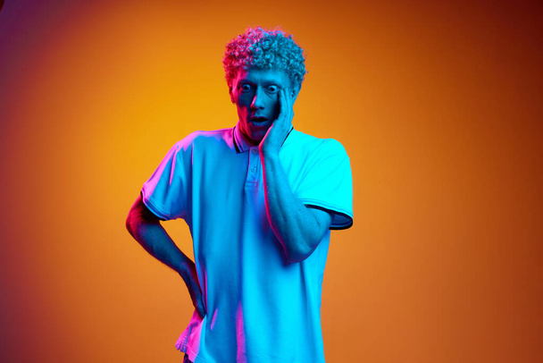 Portrait of mature man with wide open eyes expressing shock and surprise against orange studio background in blue neon light. Concept of human emotions, lifestyle, youth, facial expression - Photo, image