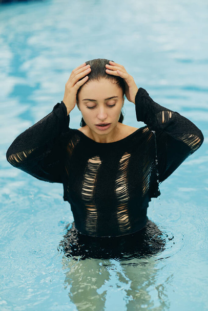 no makeup look, beautiful and sexy woman in black knitted outfit posing inside of outdoor swimming pool during vacation in Miami, alluring, luxury resort, natural beauty  - Photo, Image