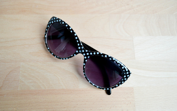 Black and white sunglasses with violet lenses on a wooden table closeup - Photo, Image