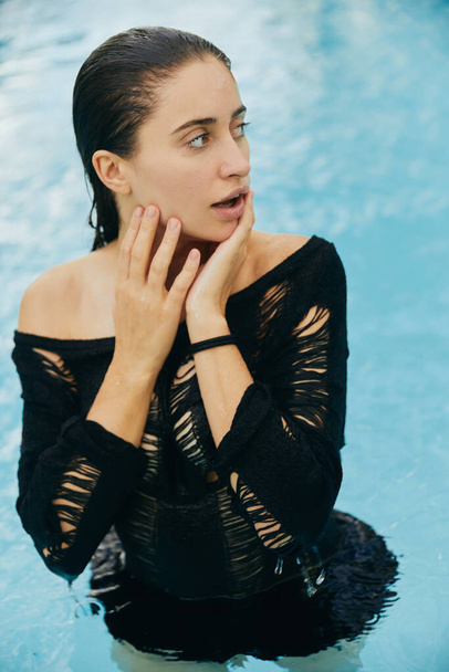 resort de luxe à Miami, femme embrassée par le soleil avec peau bronzée touchant son visage humide après avoir nagé dans la piscine publique, posant et profitant de ses vacances d'été, sans maquillage  - Photo, image