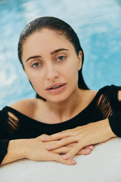 resort de luxe à Miami, belle femme avec peau bronzée regardant la caméra, à l'intérieur de la piscine publique, posant et profitant de ses vacances d'été, sans maquillage, portrait  - Photo, image