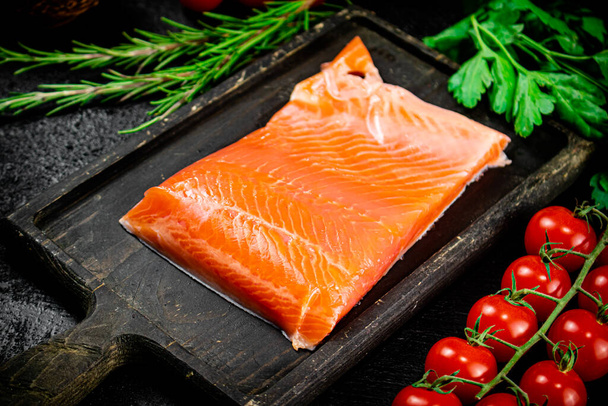 Salted salmon with greens and tomatoes on a cutting board. On a black background. High quality photo - Фото, зображення