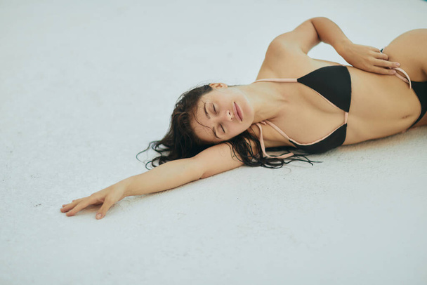 csábító nő fekete bikini, szexi modell nedves haj pózol luxus üdülőhely, Miami, Florida, USA, elmosódott háttér, feküdt a fehér felületen, medence melletti pihenés  - Fotó, kép