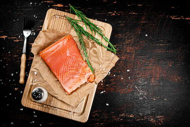 A piece of salted salmon on a cutting board with rosemary and spices. Against a dark background. High quality photo - Фото, зображення