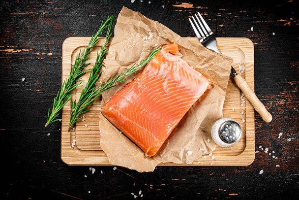 A piece of salted salmon on a cutting board with rosemary and spices. Against a dark background. High quality photo - Фото, зображення