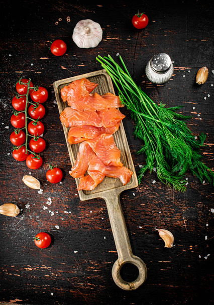 Slices of salted salmon on a cutting board with dill and tomatoes. Against a dark background. High quality photo - Φωτογραφία, εικόνα