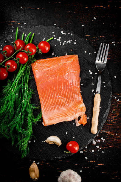 A piece of salted salmon with tomatoes and greens on a stone board. On a rustic with a dark background. High quality photo - Фото, зображення