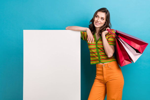 Portrait of nice woman dressed colorful cardigan arm on board look empty space hold shopping bags isolated on blue color background. - Zdjęcie, obraz