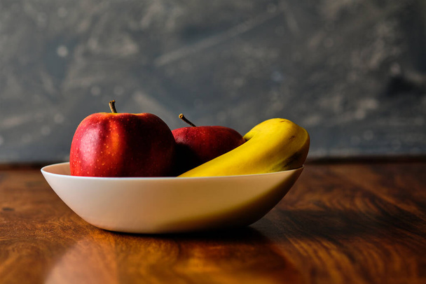 Still life with red apples and banana fruit in bowl on wooden table - Photo, Image