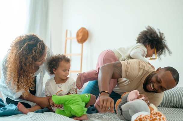 Happy African American Parents with  little daughters playing on the bed in bedroom at home, happy family concept - Фото, изображение