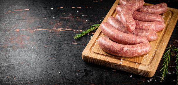 Raw sausages on a cutting board with a sprig of rosemary. On a rustic dark background. High quality photo - Foto, immagini