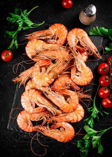 Boiled shrimp on a stone board with tomatoes and parsley. On a black background. High quality photo - Фото, изображение
