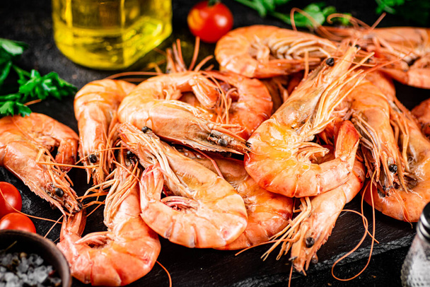Boiled shrimp on a stone board with tomatoes and parsley. On a black background. High quality photo - Фото, изображение