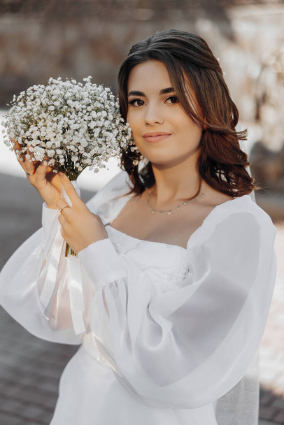 Beautiful bride perfect style. Wedding hairstyle, make-up, luxurious wedding dress and bride's bouquet. A bouquet of gypsophila. The bouquet is beautifully placed near the face. - Фото, зображення