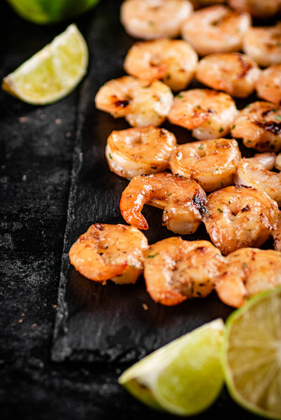 Grilled shrimp on a stone board with pieces of lime. On a black background. High quality photo - Fotó, kép