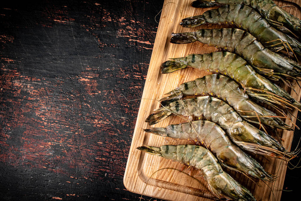 On a wooden cutting board raw shrimp. Against a dark background. High quality photo - Zdjęcie, obraz