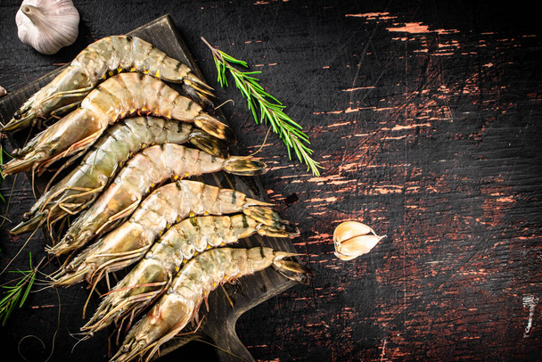 Raw shrimp on a cutting board with rosemary and garlic. Against a dark background. High quality photo - Zdjęcie, obraz