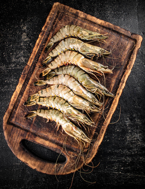 Fresh raw shrimp on a wooden cutting board. On a black background. High quality photo - Zdjęcie, obraz