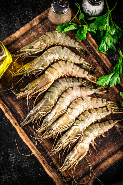 Raw shrimp on a cutting board with spices and parsley. On a black background. High quality photo - Fotografie, Obrázek