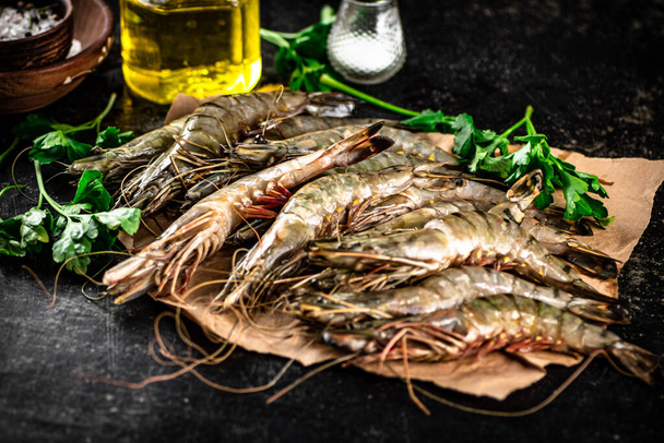Raw shrimp on paper with spices and parsley. On a black background. High quality photo - Photo, Image