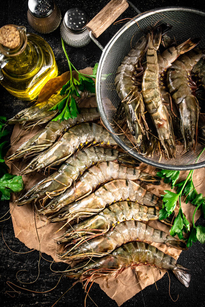 Raw shrimp on paper with spices and parsley. On a black background. High quality photo - Foto, afbeelding