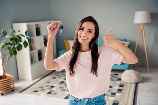 Photo of confident sweet young lady dressed pink t-shirt rising thumb up new house key indoors house room. - Photo, Image