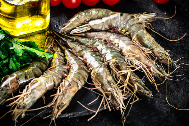 Raw shrimp on a stone board with parsley and tomatoes. On a black background. High quality photo - Фото, изображение