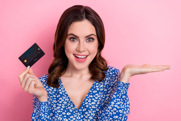 Portrait of cute impressed girl wear blue blouse hold debit card palm demonstrate offer empty space isolated on pink color background. - Zdjęcie, obraz