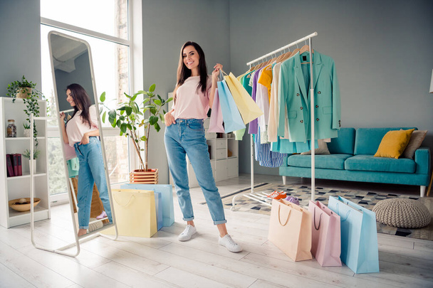 Photo of cheerful positive young lady dressed pink t-shirt holding shoppers choosing new outfits indoors house room. - Fotó, kép