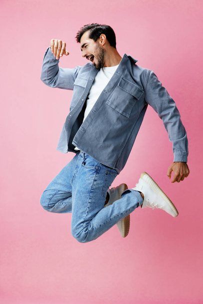 Άνδρας με γενειάδα να πηδάει σε ροζ φόντο με λευκό μπλουζάκι και τζιν, χαμόγελο και χαρούμενη συγκίνηση στο πρόσωπό του, ολόσωμος, αντιγραφικός χώρος. Υψηλής ποιότητας φωτογραφία - Φωτογραφία, εικόνα