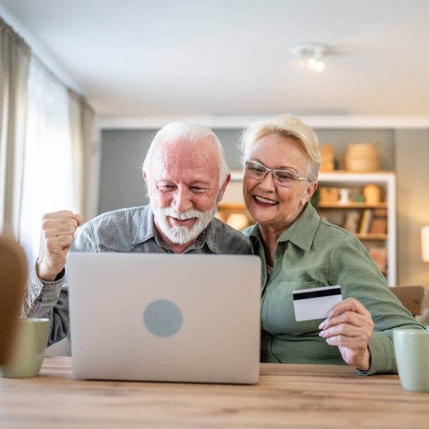 couple mature senior women and man husband and wife sit at home use credit or debit card for online shopping browse internet stores buying stuff use laptop computer real people copy space - Foto, imagen