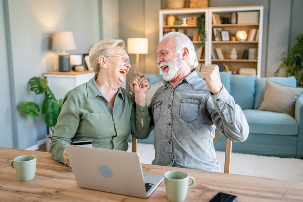 couple mature senior women and man husband and wife sit at home use credit or debit card for online shopping browse internet stores buying stuff use laptop computer real people copy space - Photo, Image