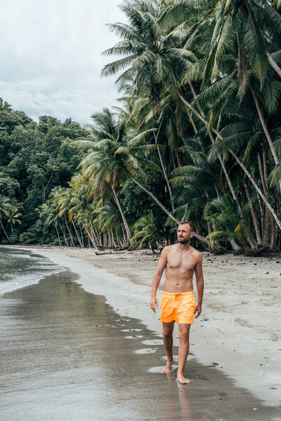 Όμορφος, υγιής άντρας που περπατάει στην παραλία και κοιτάζει προς τη θάλασσα.  - Φωτογραφία, εικόνα
