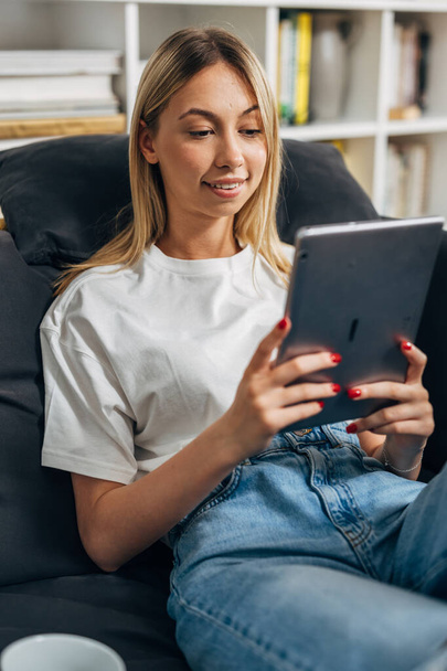 A blond Caucasian woman is relaxing at home while looking at tablet - Photo, Image