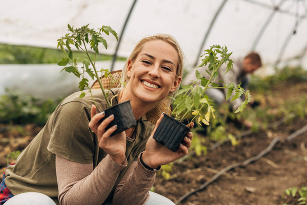 A beautiful happy woman poses with 2 tomato seedlings next to her face. - Fotografie, Obrázek