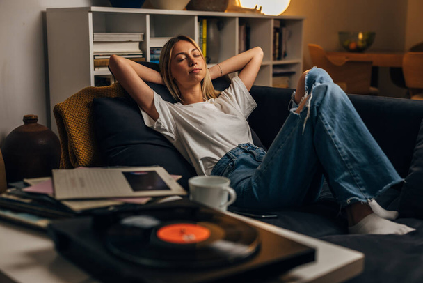 a blond woman is listening to vinyl records and relaxing. - Valokuva, kuva