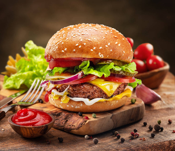 Tasty cheeseburger or hamburger on wooden tray, spices and vegetables near it. - Fotoğraf, Görsel